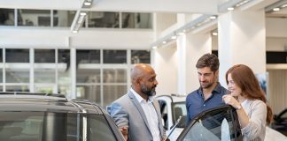 5 unique customer experience best practices to try this year Mature salesman delivering an excellent customer experience to a man and woman in car dealership showroom.