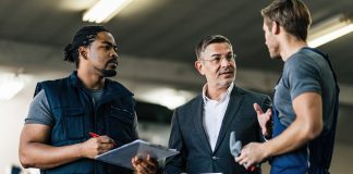 From overwhelmed to aligned action: Empowering service advisors for success Mid adult manager using digital tablet while talking to service advisors in auto repair shop.